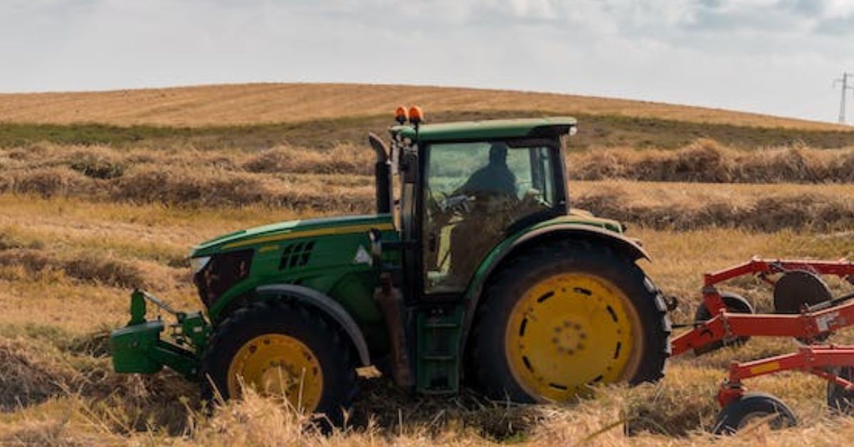 A green farm tractor is working in fields